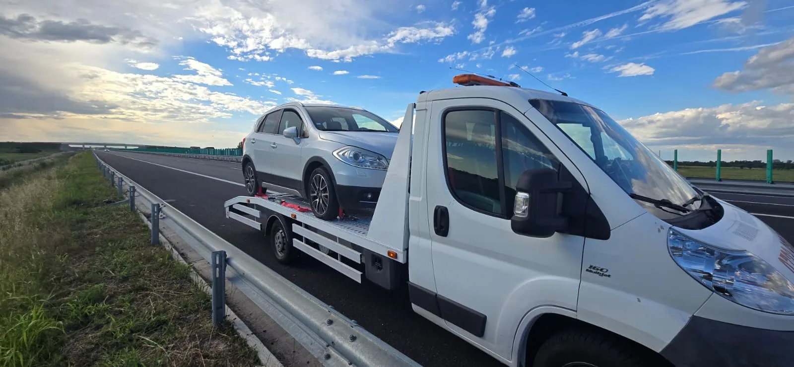 Platforma albă a firmei, cu un SUV argintiu, pe marginea unui drum de mare viteză