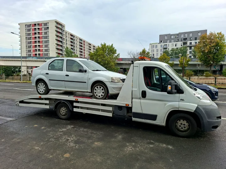 Platformă albă cu un autoturism transportat, fotografiată ziua
